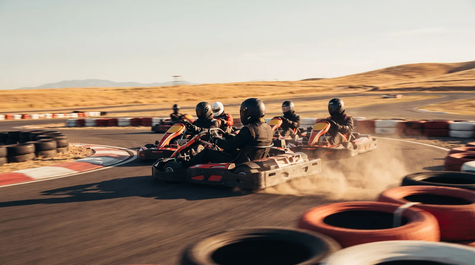 Six racing karts sliding wheel to wheel through a corner on the kart circuit, dust rising, helmets down